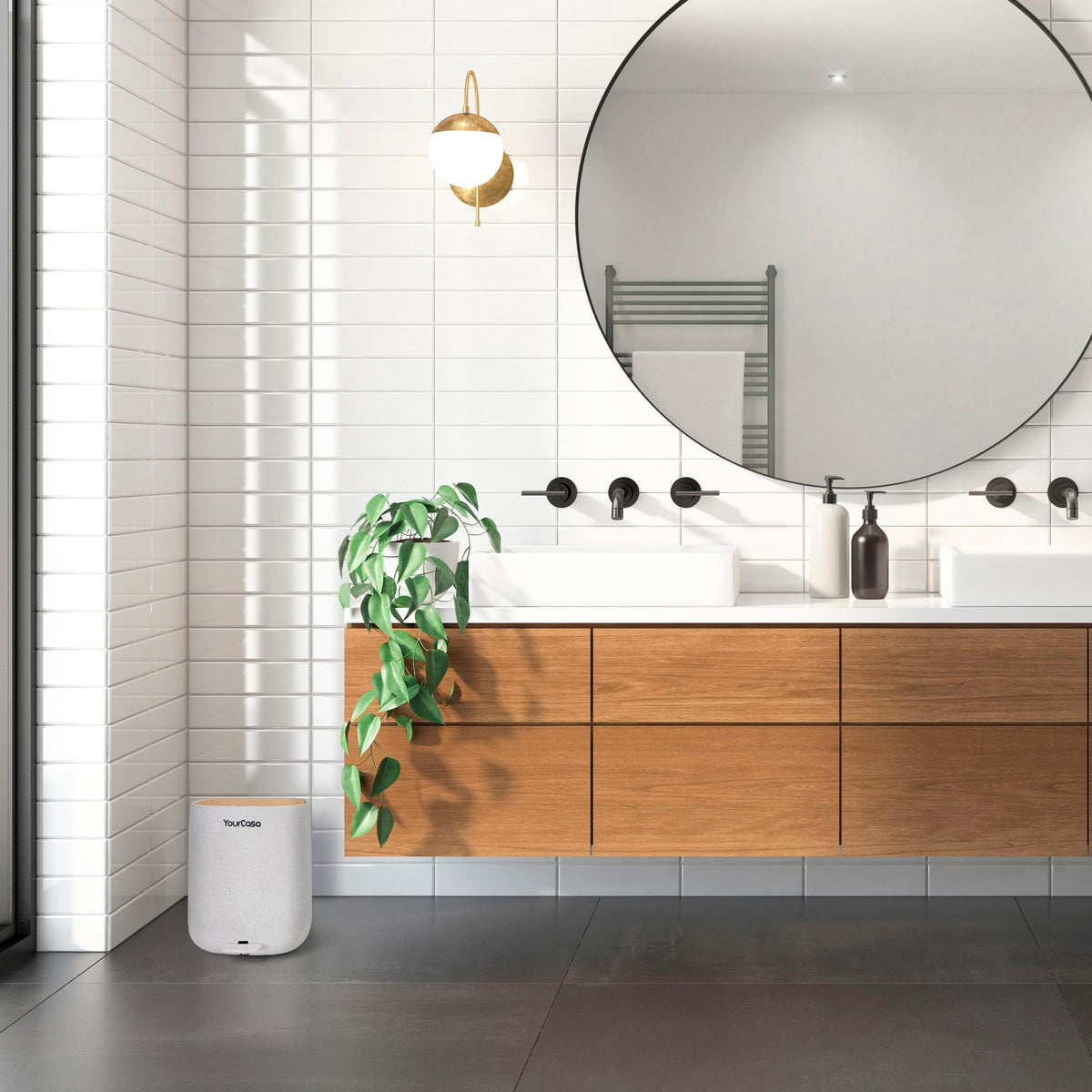 Ein modernes Badezimmer mit großem runden Spiegel, Holzschrank, Doppelwaschbecken, Wandlampe und Pflanze auf einem YourCasa® Mülleimer [5L] von yourcisade.com. Der Mülleimer reduziert den Plastikverbrauch um 30 % und besticht durch sein elegantes Design, das sich für Badezimmer oder Küchen eignet. Weiß geflieste Wände und ein dunkler Fliesenboden sorgen dafür, dass der Raum schimmelfrei und stilvoll umweltfreundlich bleibt.