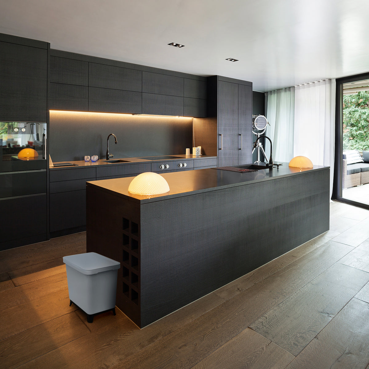 Moderne Küche mit dunklen Schränken, integrierten Geräten und einer Insel mit Pendelleuchte und einem YourCasa® Mülltrennsystem mit 2-4 Fächern [20-40L] – Effiziente Mülltrennung mit exklusivem Design von yourcisade.com.