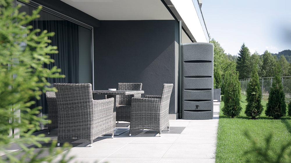 Moderne Terrasse mit Korbmöbeln mit Blick auf eine Wiese mit YourCasa Regentonne [EcoTower] – Platzsparend und Stilvoll – 260 und 720 Liter von yourcisade.com und Bäumen.