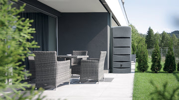 Moderne Terrasse mit Korbmöbeln mit Blick auf eine Wiese mit YourCasa Regentonne [EcoTower] – Platzsparend und Stilvoll – 260 und 720 Liter von yourcisade.com und Bäumen.