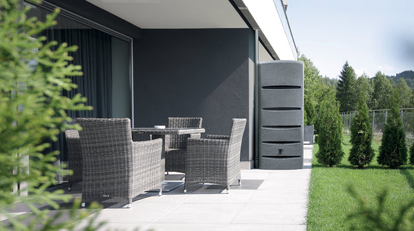 Moderne Terrasse mit Korbmöbeln mit Blick auf eine Wiese mit YourCasa Regentonne [EcoTower] – Platzsparend und Stilvoll – 260 und 720 Liter von yourcisade.com und Bäumen.