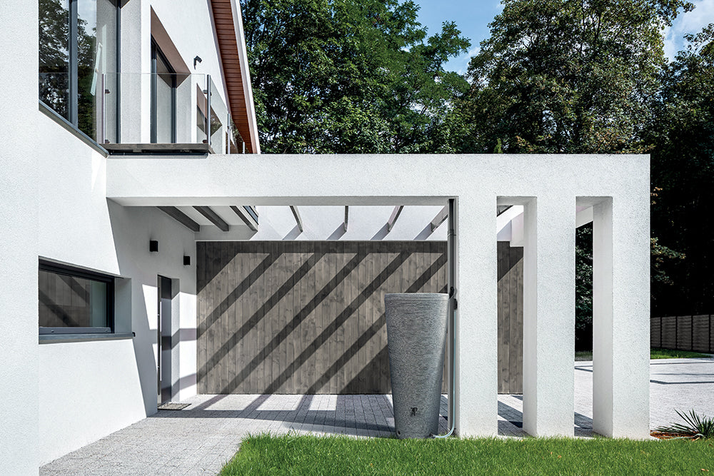 Ein modernes weißes Haus mit einer Holzveranda und einem Tubo-Tank 320 Liter – Robuste Regentonne mit großem Fassungsvermögen und stilvollem Design im Garten von yourcisade.com.